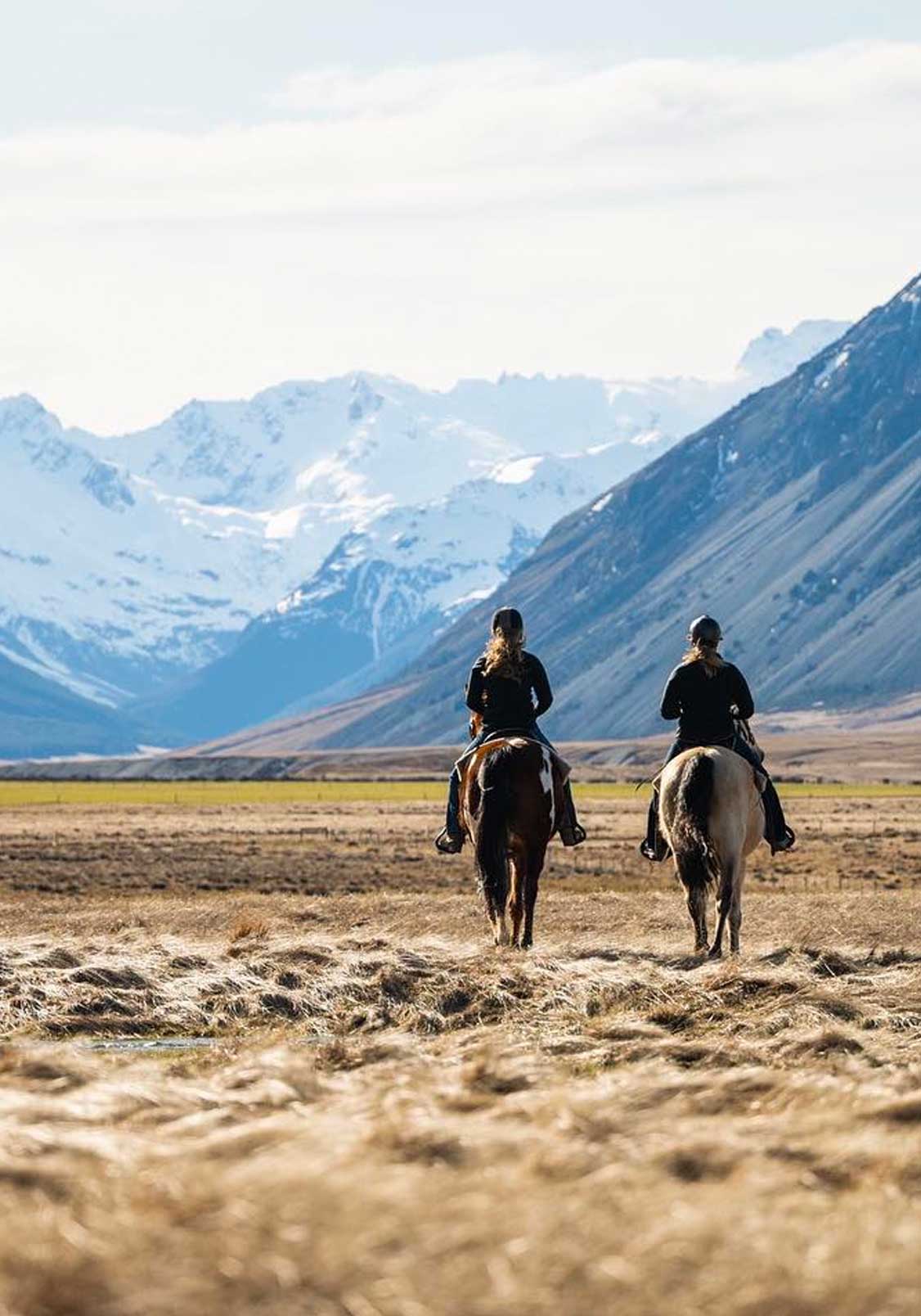 Two people horseback riding in a scenic valley in New Zealand.