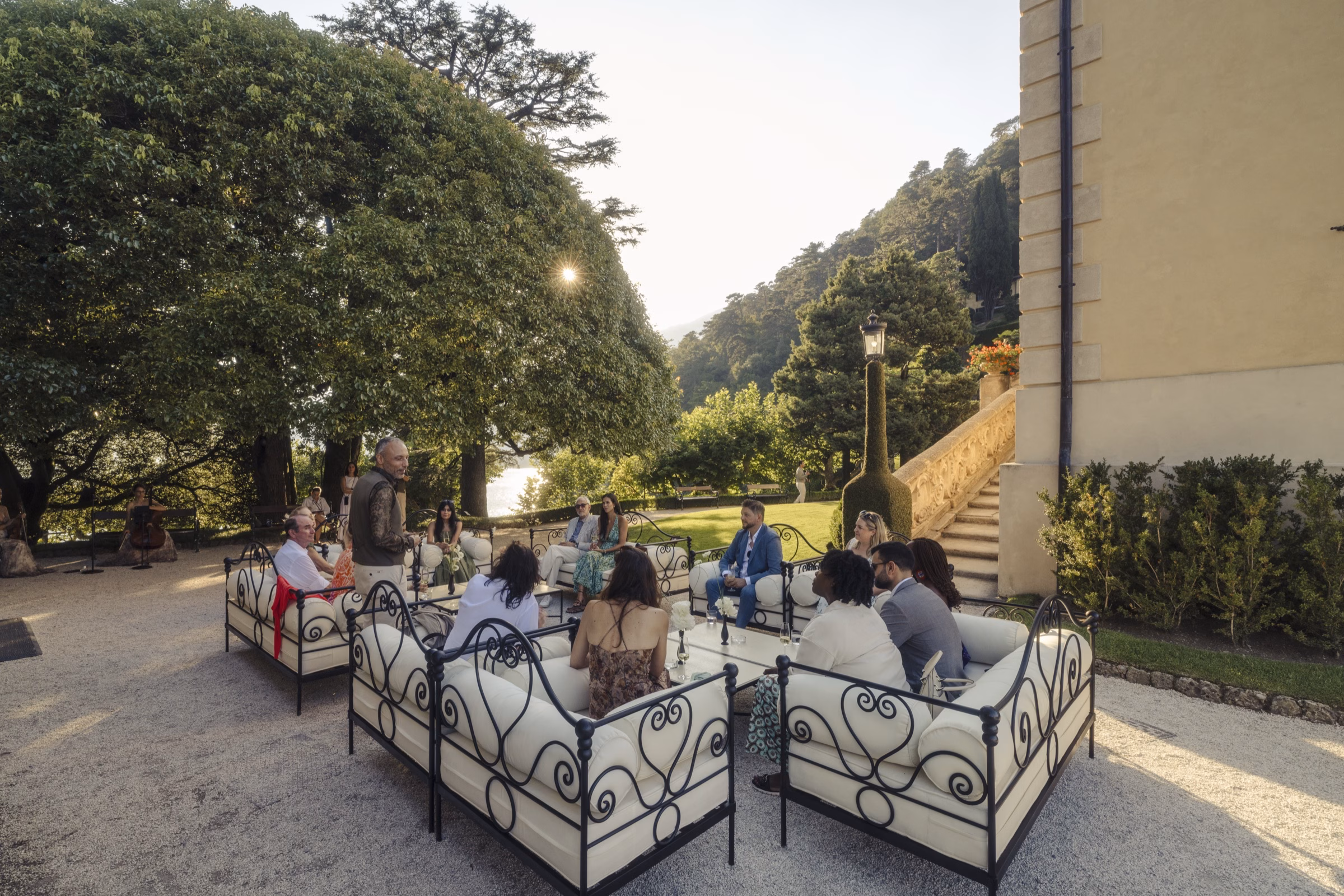 Guests gathered on wrought-iron sofas for a Foundation Circle in the gardens of a Lake Como villa at golden hour